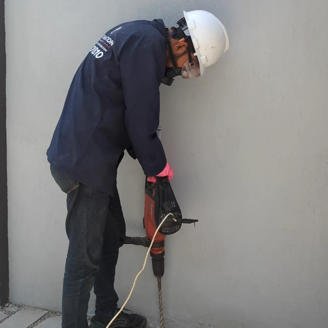 Technician in safety gear drilling termite injection holes at a boundary wall base in Karachi
