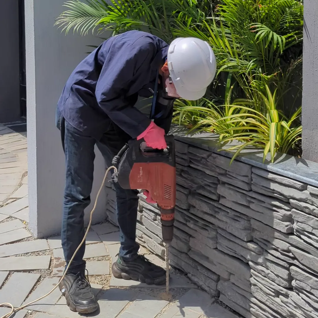 Technician drilling termite injection holes along a villa boundary planter wall in Karachi